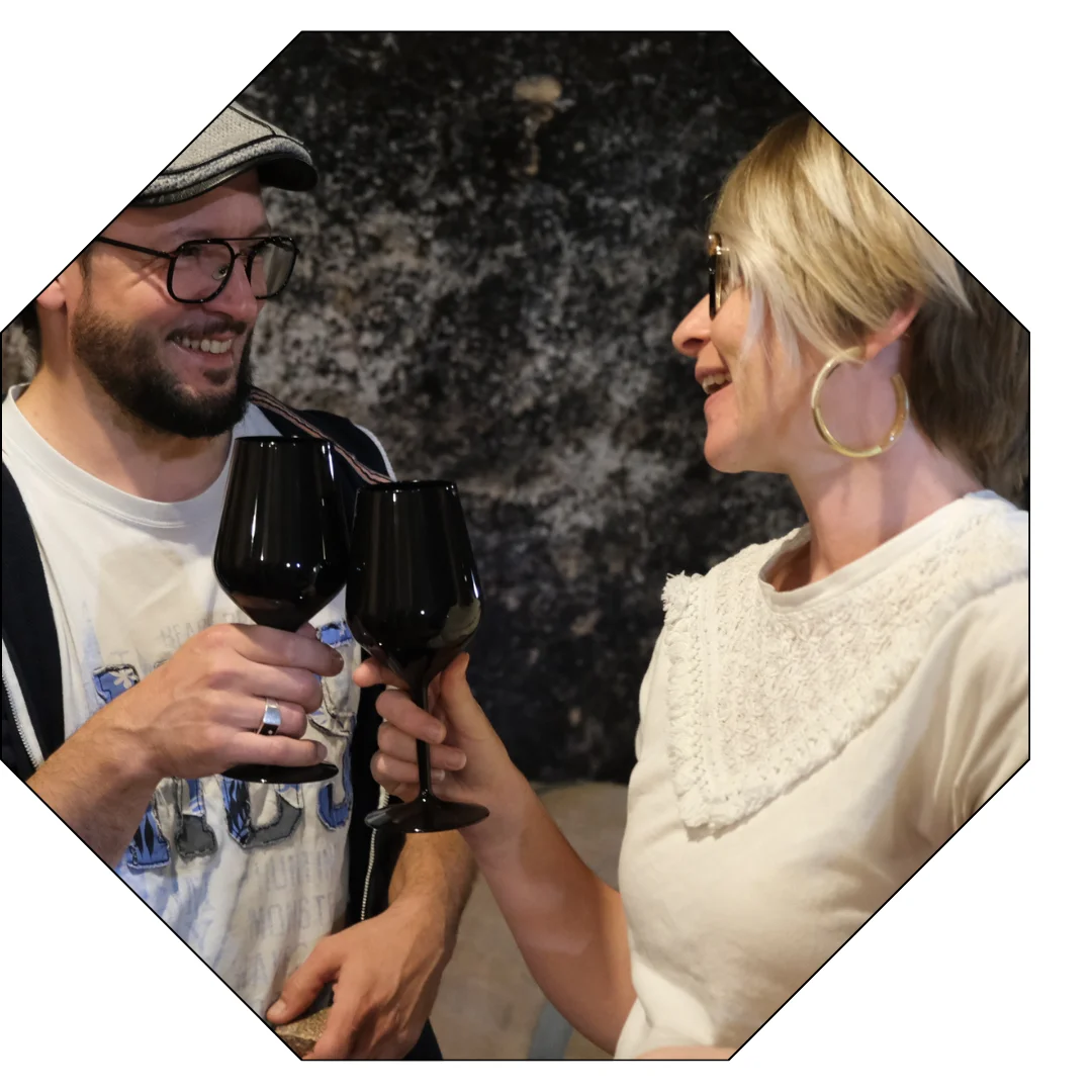 Dans une cave voutée d'un château, un couple complice et souriant trinquent lors d'un atelier géo sensoriel.