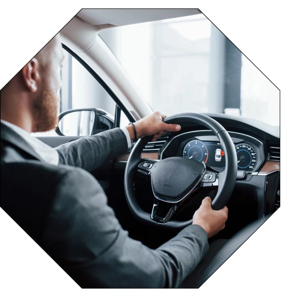 Un homme en costume élégant au volant d’une voiture de luxe, symbole d’un service de transport haut de gamme pour une expérience œnotouristique immersive et sur-mesure