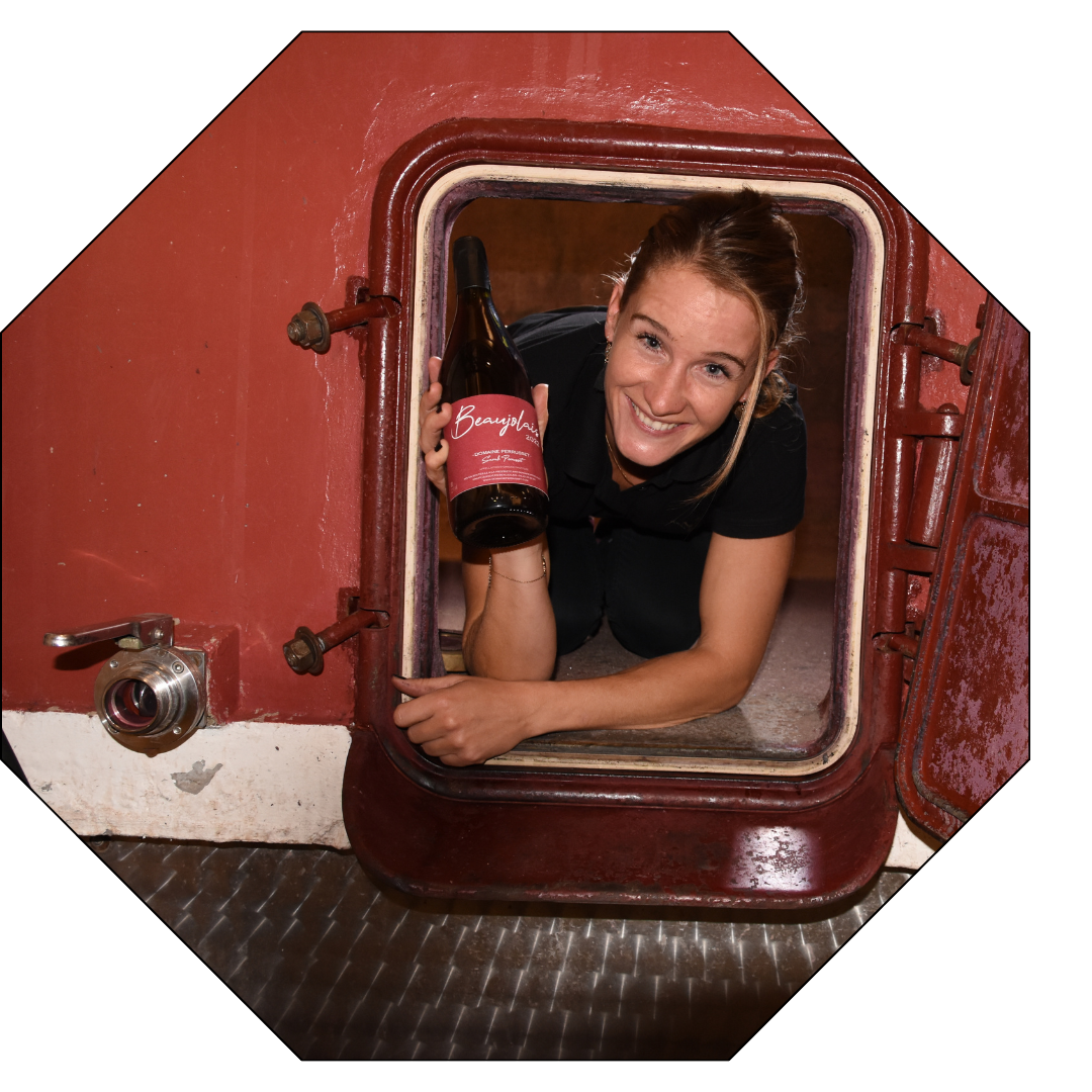 Sarah Perrusset, vigneronne passionnée du Beaujolais, souriante dans son chai, tenant une bouteille de vin issu de son domaine viticole familial.