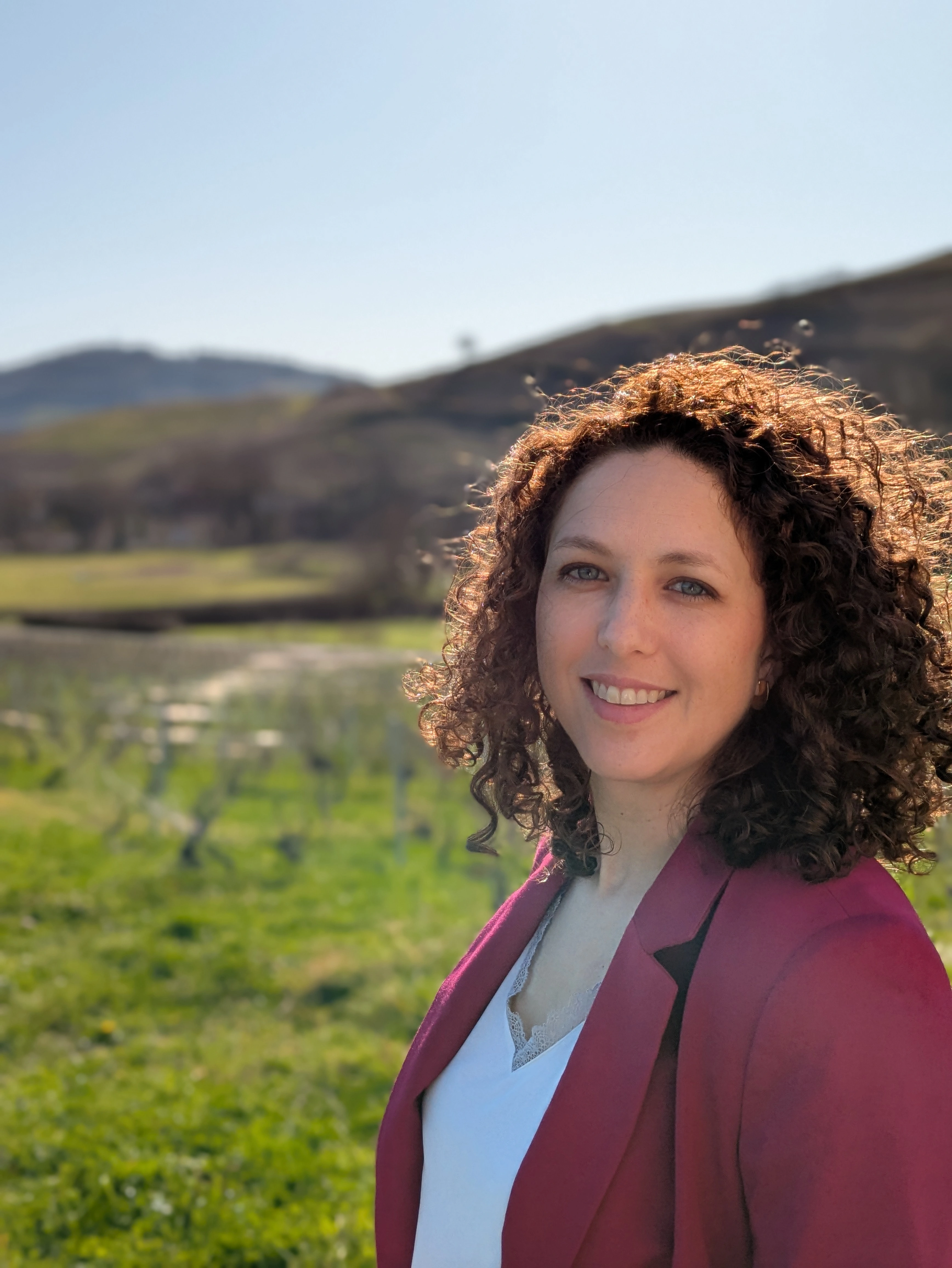 Portrait d'Inès DELMOTTE, cofondatrice de Les Epicurieuses dans les vignes du Beaujolais avec une veste rose.
