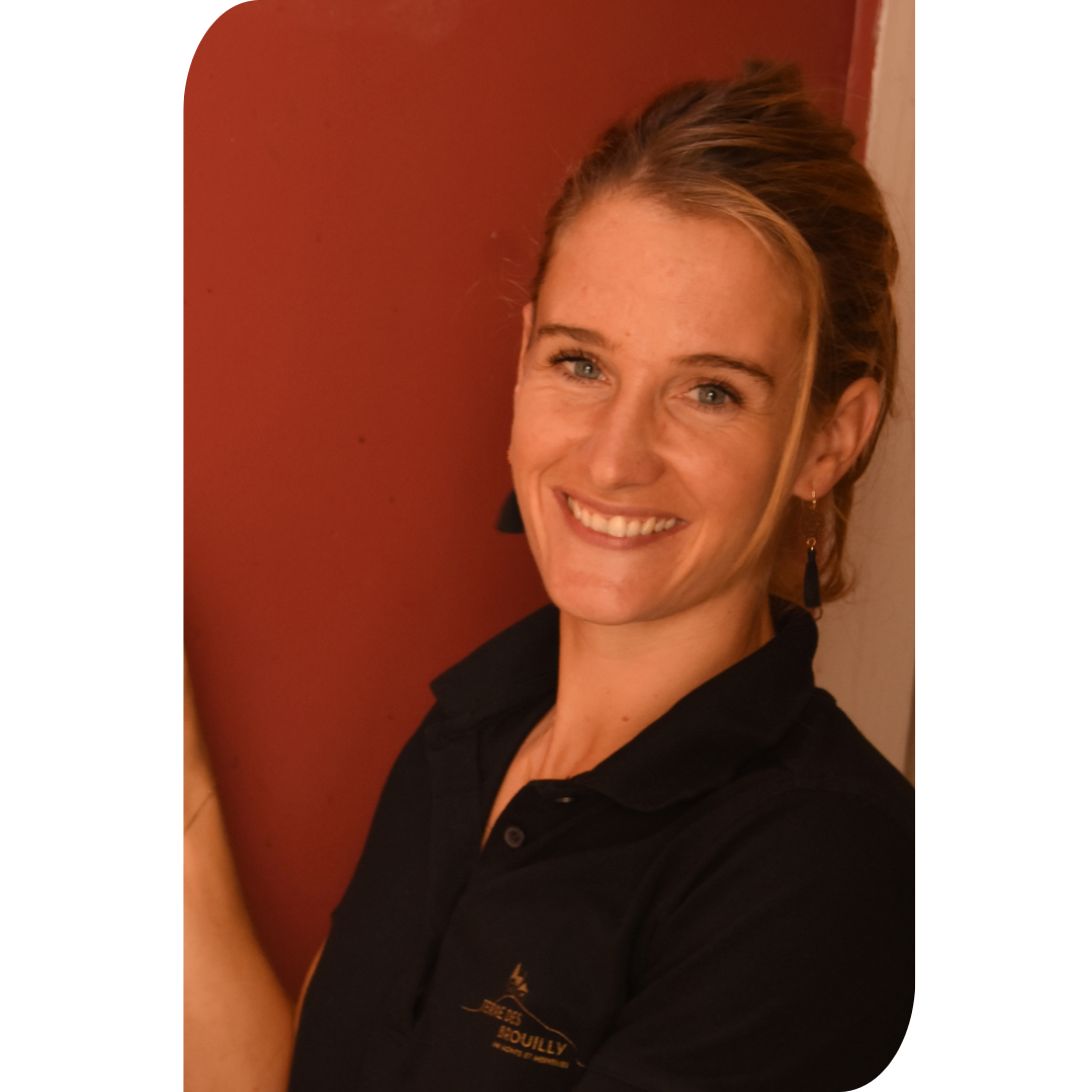 Sarah Perrusset, jeune vigneronne du Beaujolais, souriante dans son chai, remplit un verre de vin rouge directement depuis une cuve, incarnant la passion et le dynamisme d’une nouvelle génération de vignerons.