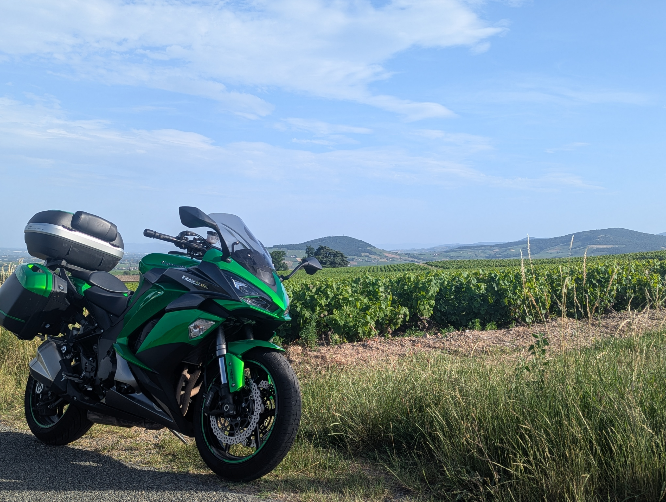 Moto de tourisme stationnées en bordure de vignoble dans le Beaujolais avec une vue panoramique sur le mont brouilly et les vignes.