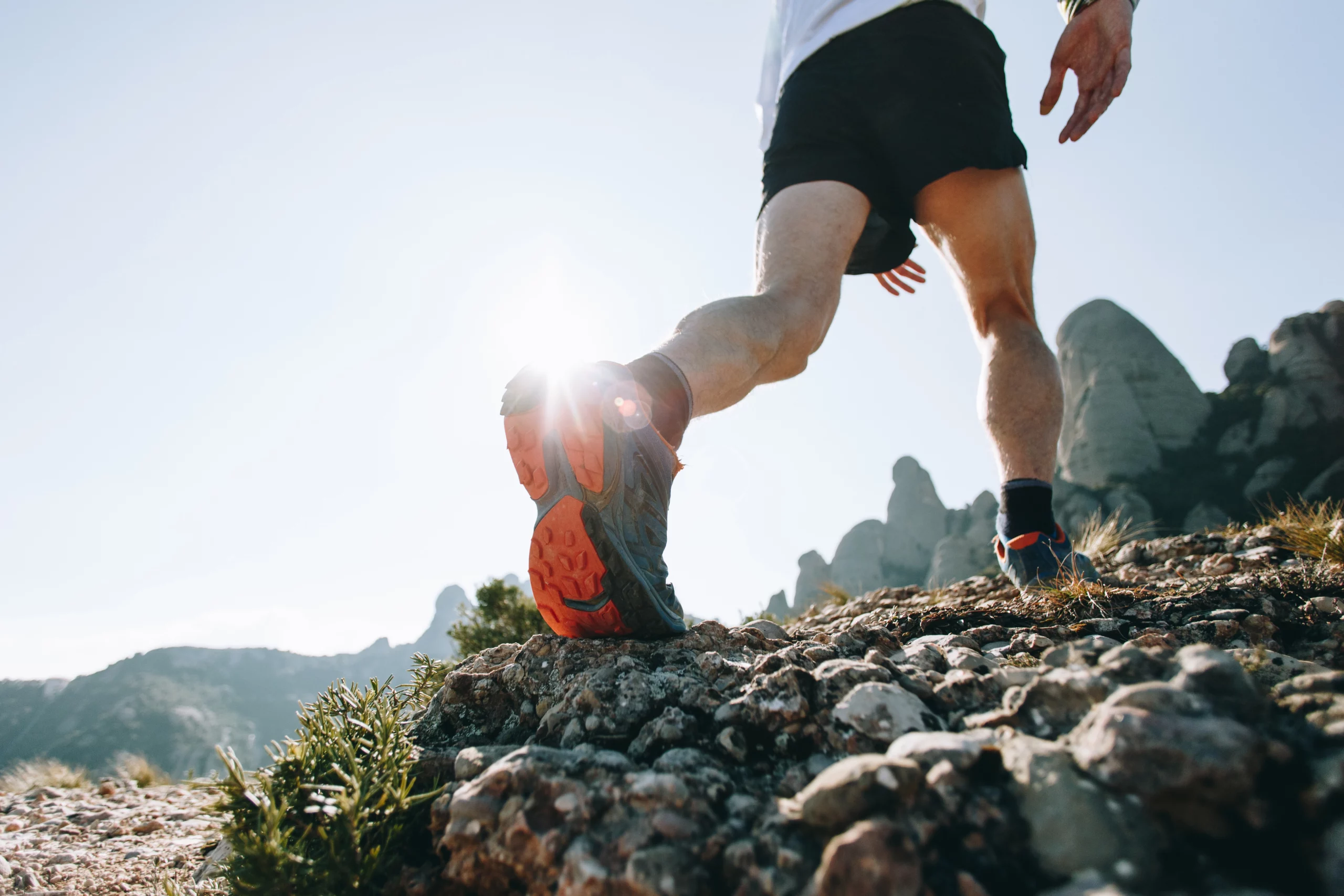 Coureur de trail en pleine ascension sur un terrain rocheux et ensoleillé dans les monts du Beaujolais, proche de Lyon.